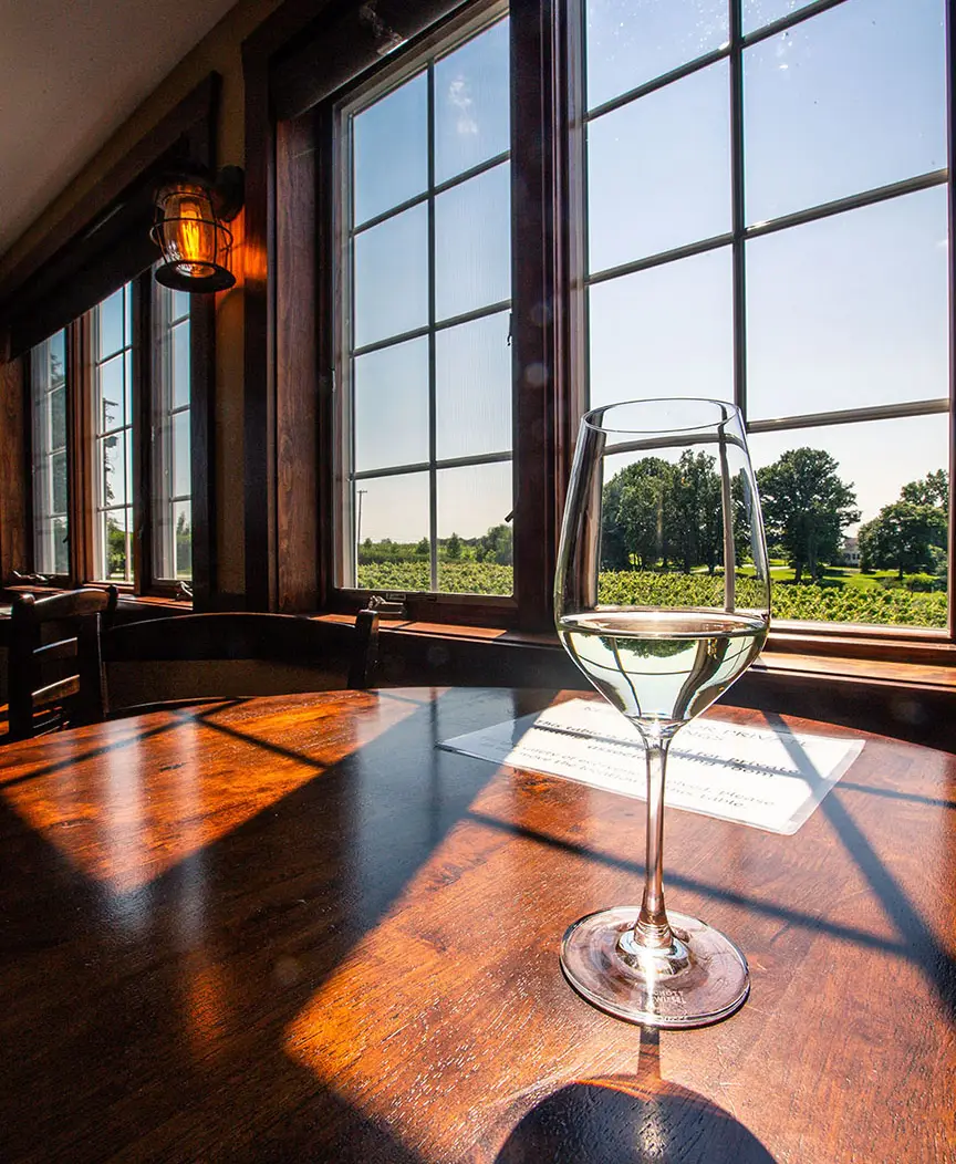 A glass of white wine on a tasting room table overlooking a Northeast Ohio vineyard